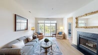 Located at 2215 Hailey Dr in Marlton, NJ, this well-appointed 2-bedroom, 2-bathroom single-floor residence offers a thoughtfully designed layout filled with natural light and comfortable living spaces. The open living room is a standout, featuring large sliding glass doors that lead to a private balcony and flood the space with natural light and tree-lined views. Light hardwood-style flooring runs throughout the main living areas, complementing the clean, neutral color palette. A decorative fireplace with an elegant mantle serves as a focal point between the living and dining areas, adding warmth and charm. The dining room is defined by vaulted ceilings and a classic pendant chandelier, creating an inviting atmosphere for gatherings. The kitchen is equipped with warm wood cabinetry, a skylight for added brightness, and white appliances, including a dishwasher and range. The spacious primary bedroom features plush carpeting and generous closet space, with a total of six closets throughout the residence ensuring ample storage. A dedicated in-unit laundry room houses a full-size washer and dryer. The bathrooms are clean and functional, featuring a tub-shower combination. The private balcony, accessible from the living room, offers a relaxing outdoor retreat with a covered pergola-style overhead structure.