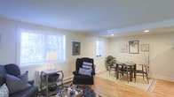 Located at 1650 West Chester Pike in West Chester, Pennsylvania, this single-floor space offers a welcoming and well-appointed interior that balances comfort with functionality. The open layout seamlessly connects a living area and dining space, creating a cohesive flow throughout the main living area. Warm hardwood floors run throughout, adding a classic and timeless character to the space. Large windows on multiple walls flood the interior with abundant natural light, enhancing the bright, airy atmosphere and offering pleasant views of the surrounding greenery. The living area is thoughtfully arranged, with recessed lighting complementing the natural illumination from the windows. Neutral wall tones provide a clean, versatile backdrop throughout. The adjacent dining area accommodates a full dining table and chairs, making it well-suited for both everyday meals and gatherings. Baseboard heating is present throughout, ensuring year-round comfort. Tasteful wall art and greenery add warmth and personality to the space. Overall, the interior presents a calm, inviting ambiance with a practical single-floor layout ideal for easy living and navigation.