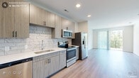 Located at Slater Crossing in Morrisville, NC, this thoughtfully designed one-bedroom, one-bathroom residence offers a clean, contemporary aesthetic throughout its efficiently laid-out single floor. Light wood-look flooring flows seamlessly across every room, creating a cohesive and bright interior.

The kitchen is a standout feature, showcasing light wood cabinetry with matte black hardware, a marble-style subway tile backsplash, white quartz countertops, and a full suite of stainless steel appliances including a range, over-the-range microwave, dishwasher, and French door refrigerator. Recessed lighting adds a polished finish to this well-equipped cooking space.

The open living area extends naturally toward a sliding glass door that opens onto a private balcony overlooking lush, wooded greenery — bringing the outdoors in with an abundance of natural light.

The generously sized bedroom features multiple windows framing tree-lined views, a ceiling fan, and direct access to the bathroom. The bathroom is appointed with a wood-toned vanity, white quartz countertop, framed mirror, and a walk-in shower.

A dedicated laundry area with a stacked washer and dryer and overhead shelving rounds out this well-appointed residence, offering convenient in-unit functionality.