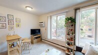 Located at 615 SE 15th Ave in Minneapolis, MN, this one-bedroom, one-bathroom unit offers a practical and well-organized layout across a single floor. An entry hallway with textured walls leads into the combined living area, where large windows flood the carpeted space with natural light and offer views of the surrounding greenery. The living room provides a relaxed atmosphere, featuring baseboard heating, a wall-mounted air conditioning unit, and ample room for seating and a small dining setup. A galley-style kitchen runs adjacent to the living area and is equipped with warm wood cabinetry, a gas range, a full-size refrigerator, and tile flooring, making efficient use of the available space. The bedroom is a comfortable, light-toned retreat with soft carpet, a woven pendant light fixture, and enough space for a full bed and dresser. The bathroom features classic white beadboard wainscoting, a mirrored medicine cabinet, a pedestal-style vanity, and a shower/tub combination with a neutral striped curtain, offering a clean and simple aesthetic. Throughout the unit, the overall ambiance is bright, functional, and inviting — well-suited for those seeking a compact yet complete living space in the heart of Minneapolis.