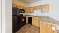 This single-floor residence offers a clean, practical layout designed for comfortable everyday living. The kitchen serves as a functional centerpiece, showcasing warm knotty pine cabinetry that extends to the upper and lower walls, paired with neutral countertops and a peninsula that provides additional prep space and casual seating. A full suite of black appliances — including a refrigerator, range, microwave, and dishwasher — completes the kitchen. The flooring throughout the kitchen and bathroom features durable stone-look tile in earthy tones, lending a grounded, cohesive aesthetic to these areas. The bedrooms are bright and inviting, each finished with plush neutral carpeting and windows fitted with blinds that allow for adjustable natural light. The rooms offer a clean, versatile canvas suitable for a variety of furnishing arrangements. The bathroom is thoughtfully appointed with a knotty pine vanity that matches the kitchen cabinetry, a warm countertop with an undermount sink, and a full-size soaking tub with a shower surround enclosed in crisp white. The consistent use of natural wood tones and neutral wall colors throughout the space creates a cohesive, understated aesthetic that feels both welcoming and easy to personalize.