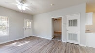 This single-floor residence offers a clean, neutral aesthetic throughout, with light gray walls and white trim creating a bright, cohesive look across all rooms. The open living and dining area is finished with durable wood-look flooring and features a ceiling fan, multiple windows with natural light, and a convenient built-in desk with granite-style countertop — ideal as a home office nook. A pendant chandelier adds a touch of elegance to the dining transition space. The galley-style kitchen is efficiently designed with white cabinetry, granite-look countertops, a stainless steel sink, and black appliances including a range, microwave, and refrigerator. Wood-look flooring continues throughout the kitchen for easy maintenance. The bedrooms are carpeted for comfort and each includes a ceiling fan. One bedroom offers two closets and a window with natural light. The bathroom is notably spacious, featuring a long double-vanity with white cabinetry and granite-look countertops, wood-look flooring, and a separate water closet with additional storage cabinetry above. A windowed exterior entry door with a sidelight adds charm to the main entrance, which connects directly to the living area. Overall, the space presents a functional and move-in-ready layout with consistent finishes throughout.