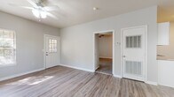 This single-floor residence offers a clean, neutral aesthetic throughout, with light gray walls and white trim creating a bright, cohesive look across all rooms. The open living and dining area is finished with durable wood-look flooring and features a ceiling fan, multiple windows with natural light, and a convenient built-in desk with granite-style countertop — ideal as a home office nook. A pendant chandelier adds a touch of elegance to the dining transition space. The galley-style kitchen is efficiently designed with white cabinetry, granite-look countertops, a stainless steel sink, and black appliances including a range, microwave, and refrigerator. Wood-look flooring continues throughout the kitchen for easy maintenance. The bedrooms are carpeted for comfort and each includes a ceiling fan. One bedroom offers two closets and a window with natural light. The bathroom is notably spacious, featuring a long double-vanity with white cabinetry and granite-look countertops, wood-look flooring, and a separate water closet with additional storage cabinetry above. A windowed exterior entry door with a sidelight adds charm to the main entrance, which connects directly to the living area. Overall, the space presents a functional and move-in-ready layout with consistent finishes throughout.