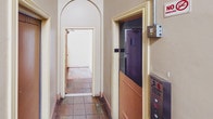 This single-floor space presents a thoughtfully designed layout with a mix of classic architectural elements and practical features. The standout feature is a long, narrow corridor finished with rich, warm-toned hardwood flooring that runs the length of the building, lined with neutral-painted walls and overhead track lighting that draws the eye toward the far end. Multiple doorways along the corridor provide access to individual rooms or units.

A staircase landing area connects key zones within the space, featuring a traditional wooden staircase with cream-painted balusters and a polished handrail, complemented by matching hardwood flooring and bright overhead fluorescent lighting. Adjacent to the staircase, a doorway opens into a secondary passage, also finished with hardwood floors.

The tiled entryway area offers a transition point with neutral floor tiles and cream-colored walls. A distinctive arched doorway serves as an elegant architectural accent, framing the passage between areas and adding a touch of classic character. An elevator is also present, enhancing accessibility throughout the building.

Throughout the space, the consistent use of cream and neutral tones, combined with warm wood flooring and traditional trim details, creates a cohesive and understated aesthetic suited to a multi-room building environment.