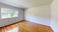 This multi-floor residence in Norwich, CT offers a well-organized layout spread across three floors, providing distinct living zones and comfortable separation between spaces. The main living level features a functional kitchen equipped with warm oak cabinetry, granite-style countertops, a double sink, and white appliances including a range and dishwasher, alongside light wood-look flooring and a window that brings in natural light. The living room continues the bright, open aesthetic of the main floor. Upstairs, two bedrooms feature gleaming hardwood floors and windows with outdoor views of surrounding greenery, offering a warm and inviting atmosphere. The spacious primary bedroom provides generous room for furnishings. The two bathrooms include a full bath with a tiled tub/shower surround, chrome fixtures, and a wall mirror cabinet, as well as a secondary bathroom with light wood-look flooring, a wall-mounted sink, and a mirrored medicine cabinet. The lower level offers a large open area with painted concrete floors and painted walls, suitable for storage or utility use, accessed via a staircase with a wooden handrail. Baseboard heating is present throughout, ensuring year-round comfort.