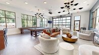 Located in Winston-Salem, NC, this thoughtfully designed amenity space offers a dynamic and engaging environment for socializing and recreation. The open, single-floor layout maximizes functionality while maintaining a cohesive, upscale aesthetic throughout.

The game room area is a standout feature, anchored by a full-size pool table and a ping pong table, with large glass garage-style doors that open to an outdoor terrace, seamlessly blending indoor and outdoor living. Multiple flat-screen TVs are positioned throughout for entertainment.

The lounge area exudes contemporary sophistication, featuring a rich cognac leather sofa, curved accent chairs, and a round gold coffee table arranged atop a neutral area rug. A dramatic marbled blue accent wall serves as a bold focal point, complemented by an artistic geometric console table and coordinating table lamps beneath a wall-mounted TV.

The bar and dining nook is defined by floor-to-ceiling industrial-style windows that flood the space with natural light and offer sweeping outdoor views. A long white quartz bar counter with warm wood detailing is paired with sleek black and gold bar stools, creating an inviting space for casual gatherings.

Rich hardwood flooring, sculptural multi-arm chandeliers in brass and black, and recessed lighting tie the entire space together with a refined, modern sensibility.