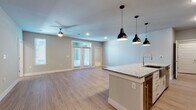 This single-story home in Dripping Springs, Texas offers a thoughtfully designed open-concept layout that seamlessly connects the kitchen, dining, and living areas. The kitchen serves as a central focal point, showcasing bold navy shaker-style cabinetry that extends to the ceiling for maximum storage, complemented by granite countertops, a subway tile backsplash, and stainless steel appliances including a French door refrigerator and built-in microwave. A large kitchen island with an undermount sink and pendant lighting provides both workspace and casual seating. Light wood-style flooring extends throughout the main living areas, while recessed lighting and ceiling fans maintain a bright, comfortable atmosphere. French doors in the living area invite natural light and provide outdoor access. The bedrooms feature plush carpeting and ceiling fans, with one room offering built-in shelving for added functionality. Walk-in closets are generously sized and outfitted with multi-tiered shelving and hanging rods. Bathrooms feature tile flooring, white cabinetry, and granite countertops. A dedicated laundry space accommodates a full-size washer and dryer with overhead shelving. Neutral gray walls and clean white trim throughout create a cohesive, modern aesthetic.