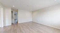 Located at 156 W Hill Ave in Fullerton, California, this single-floor, one-bedroom, one-bathroom residence offers a thoughtfully designed layout with a clean, contemporary aesthetic throughout. Light-toned, wood-look flooring runs continuously across the living spaces, complementing the neutral white and beige walls to create a bright, cohesive interior.

The combined kitchen and living room area provides an open, functional gathering space. The kitchen is equipped with white shaker-style cabinetry, light quartz countertops, and stainless steel appliances including a gas range and over-the-range microwave. Recessed lighting throughout the unit adds to the airy ambiance.

The spacious primary bedroom features a window with natural light, a wall-mounted air conditioning unit, and a generously sized closet with built-in hanging rods. An additional closet provides extra storage.

The bathroom is finished with a white shaker vanity, quartz countertop, brushed nickel fixtures, a framed mirror, and a shower-tub combination. An outdoor balcony with a metal railing offers views of the surrounding tree-lined neighborhood, adding a pleasant extension to the living space.