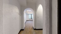 This single-floor residence showcases a charming blend of classic architectural details and functional living spaces. One of the most notable design elements is the series of elegant arched doorways that connect the hallways and rooms, adding a timeless character to the interior. The walls throughout feature a textured white finish, complemented by dark wood baseboards that provide a crisp contrast.

The living and bedroom areas are finished with wall-to-wall carpeting in a warm neutral tone, contributing to a comfortable ambiance. Several rooms benefit from natural light through windows with dark wood framing, some featuring tray-style recessed ceiling details that add visual depth. A bedroom includes a built-in shelved closet, offering practical storage.

The kitchen is well-appointed with white shaker-style cabinetry, granite-style countertops, a subway tile backsplash, and white appliances including a range and refrigerator. Light ceramic tile flooring runs through the kitchen and adjoining areas, providing easy maintenance.

The bathroom retains a distinctly vintage character, showcasing original pink ceramic wall tiles accented with dark trim, a classic pedestal sink, and a full soaking tub. A small window brings in natural light. Overall, the space presents a mix of retro charm and updated finishes throughout.