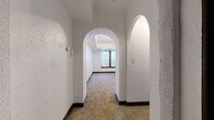 This single-floor residence showcases a charming blend of classic architectural details and functional living spaces. One of the most notable design elements is the series of elegant arched doorways that connect the hallways and rooms, adding a timeless character to the interior. The walls throughout feature a textured white finish, complemented by dark wood baseboards that provide a crisp contrast.

The living and bedroom areas are finished with wall-to-wall carpeting in a warm neutral tone, contributing to a comfortable ambiance. Several rooms benefit from natural light through windows with dark wood framing, some featuring tray-style recessed ceiling details that add visual depth. A bedroom includes a built-in shelved closet, offering practical storage.

The kitchen is well-appointed with white shaker-style cabinetry, granite-style countertops, a subway tile backsplash, and white appliances including a range and refrigerator. Light ceramic tile flooring runs through the kitchen and adjoining areas, providing easy maintenance.

The bathroom retains a distinctly vintage character, showcasing original pink ceramic wall tiles accented with dark trim, a classic pedestal sink, and a full soaking tub. A small window brings in natural light. Overall, the space presents a mix of retro charm and updated finishes throughout.