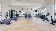 The Yardly Laveen Spectrum fitness center at 6900 S 59th Ave in Phoenix, Arizona, is a generously proportioned, single-floor exercise facility designed to support a full range of workout routines. The interior is finished with light hardwood-style flooring that reflects a clean, contemporary aesthetic, paired with crisp white walls that create a bright and energizing atmosphere throughout the space.

Large black-framed windows line the perimeter, flooding the room with abundant natural light and offering views of the surrounding outdoor amenity areas, including glimpses of a pool and palm trees. Multiple ceiling fans are suspended overhead, contributing to airflow and comfort during workouts.

The facility is comprehensively equipped with a wide array of machines and free weights. Cardio options include a row of treadmills and elliptical trainers positioned near the windowed walls. Strength training is well-represented with cable and multi-function weight machines anchoring the center of the floor, complemented by a free weights area featuring dumbbells, kettlebells, medicine balls, and a power rack with bench. A rowing machine and dedicated open floor space provide additional versatility for functional training.

Wall-mounted flat-screen televisions are positioned throughout the room for entertainment during workouts. The Yardly Laveen Spectrum branding is prominently displayed on the wall, reinforcing the facility's identity as a polished, community-focused amenity space.
