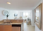 Located along the South River in Miami, FL, this thoughtfully designed high-rise unit offers a bright, open-concept layout that seamlessly blends the kitchen, dining, and living areas. The kitchen is equipped with stainless steel appliances, including a French door refrigerator, electric range, and built-in microwave, complemented by warm wood cabinetry and granite countertops. Light-toned tile flooring flows throughout, reinforcing the clean, modern feel.

The living room is a standout space, anchored by a large sectional sofa and framed by floor-to-ceiling sliding glass doors that open to a private balcony with sweeping panoramic views of the Miami skyline. A large decorative mirror amplifies the sense of space and natural light. The adjacent dining area features a wall-mounted TV and connects smoothly to the rest of the open plan.

The primary bedroom is generously proportioned with large windows that invite abundant natural light and offer scenic outdoor views, while a second bedroom maintains a serene, intimate atmosphere. Two bathrooms serve the unit — one featuring a dark-cabinetry vanity with a large mirror and tub-shower combo, and another with warm tile surround and a soaking tub. The overall ambiance is airy and coastal, with a refined yet relaxed Miami sensibility throughout.