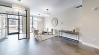 This single-floor lobby and fitness center in Boston, MA, is thoughtfully designed to provide residents with both a welcoming arrival experience and convenient wellness amenities. The entrance greets visitors with large-format tile flooring, recessed lighting, a bank of mailboxes, and elevator access, establishing a clean and functional first impression. Connecting hallways guide residents seamlessly between the various areas of the space.

The lounge area serves as a comfortable common retreat, featuring a linear fireplace with a wall-mounted television above, plush accent chairs arranged on patterned carpeting, and pendant drum lighting. Large windows allow natural light to filter in, offering views of the surrounding neighborhood and contributing to the room's welcoming ambiance. A built-in counter with cabinetry provides a beverage station for residents' convenience.

The fitness center is divided into two interconnected areas finished with durable rubber flooring. One section is appointed in a calming blue-gray palette with diagonal accent stripes and features a treadmill, stationary cycle, weight bench, and dumbbell rack. Full-length mirrors visually expand the space. The adjacent room offers additional strength training equipment and mirrors, completing a well-rounded exercise facility suited for a variety of workout routines.