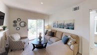This single-floor residence offers a thoughtfully designed layout with multiple bedrooms, two full bathrooms, a fully equipped kitchen, a comfortable living area, and a dedicated laundry space. The living room is bright and welcoming, featuring large sliding glass doors that open to a private balcony overlooking lush greenery, allowing natural light to fill the space. The kitchen is efficiently laid out with light wood cabinetry, white appliances including a refrigerator and electric range, a double-basin sink, and ample counter and storage space, all complemented by wood-look flooring. Each bedroom is generously sized with plush carpeting, large windows that invite natural light, and ceiling fans for added comfort. The bedrooms also feature walk-in or reach-in closet access, providing practical storage solutions. Both bathrooms are clean and functional, each offering a full tub-shower combination with tile surround, a toilet, vanity with sink, and a mirror. The dedicated laundry area is equipped with washer and dryer hookups, both electric and water connections, and an overhead wire shelving unit for storage. Overall, the space presents a comfortable and functional living environment with consistent neutral tones throughout.