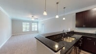 This single-floor residence is designed with an open-concept layout that connects the kitchen and living area seamlessly. The kitchen is outfitted with rich, dark espresso cabinetry, dark granite countertops, and a full suite of stainless steel appliances, including a refrigerator, range, and over-the-range microwave. A peninsula with an undermount double sink extends into the living space, complemented by three pendant lights overhead. The adjoining living area features plush carpeting, crown molding, a ceiling fan, and a multi-pane window that draws in natural light.

The bedrooms are carpeted and each include ceiling fans and windows with outdoor views, creating comfortable, well-lit retreats. The floor plan, visible in the 3D model, reveals multiple bedrooms and a practical flow throughout the unit.

Two bathrooms mirror the kitchen's design aesthetic, featuring dark espresso vanities topped with dark granite, undermount sinks, and tile flooring. One bathroom includes a shower-tub combination, while the other is a more compact layout. Both are finished with brushed nickel hardware and wall-mounted grab bars. Crown molding is present in the primary living areas, contributing to a consistently polished interior throughout.