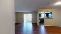 This single-floor residence offers a well-organized layout that balances open communal areas with private living spaces. The living room serves as the heart of the home, showcasing rich, dark hardwood-style flooring that extends throughout the main living areas. A full-length sliding glass door fitted with vertical blinds floods the space with natural light and provides direct access to the outdoors. Neutral-toned walls and a textured ceiling complement the warm flooring throughout.

The kitchen is thoughtfully designed with dark navy cabinetry, dark granite-style countertops, and a full suite of stainless steel and black appliances, including a refrigerator, electric range, microwave, and dishwasher. A window above the sink provides additional natural light, making the kitchen both functional and inviting.

A hallway connects the main living area to the private quarters. The bedrooms feature plush carpeting, neutral walls, and built-in closets with hanging rods, offering practical storage solutions. One bedroom includes hardwood-style flooring and a walk-in closet area. The bathroom is clean and functional, complete with a shower-tub combination and wood-look flooring. Throughout the home, consistent finishes and a neutral color palette create a cohesive and comfortable living environment.