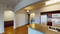 This single-floor residence offers a well-organized layout that connects living, kitchen, and private spaces in a practical and cohesive design. The open living area is finished with warm wood-look flooring and features a ceiling fan, creating a comfortable everyday environment. Natural light enters through a window and a glass-paneled exterior door, which provides direct outdoor access from the living room.

The kitchen is accessible via a defined archway and is laid out in a galley-style configuration. Dark-toned cabinetry lines both sides of the space, complemented by granite-style countertops, a stainless steel sink, and white appliances including a refrigerator, range, and dishwasher. A peninsula counter with additional seating separates the kitchen from the main living area, and a pendant light overhead adds a functional accent.

Adjacent to the kitchen, a built-in desk or utility niche provides additional workspace. The bathroom features wood-look flooring and includes a wall-mounted cabinet for storage. A separate bedroom offers its own ceiling fan, a window with blinds for natural light and privacy, and consistent wood-look flooring, maintaining a cohesive aesthetic throughout the unit.