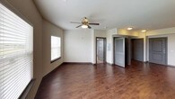 This single-floor unit presents a contemporary design aesthetic carried consistently throughout its living spaces. The open main living area features rich, dark hardwood-style flooring and neutral-toned walls, with a ceiling fan overhead and a large window fitted with blinds that invites natural light into the space. Multiple doorways connect to additional rooms, creating an accessible and functional layout.

The kitchen is a standout feature, showcasing floor-to-ceiling dark wood cabinetry with sleek bar-pull hardware, light granite countertops, and a textured tile mosaic backsplash that adds visual depth. Black stainless appliances—including a range, built-in microwave, refrigerator, and dishwasher—complete the modern culinary space. Track lighting above enhances visibility and reinforces the contemporary style.

The bedroom continues the neutral palette with wall-to-wall carpeting, a ceiling fan, and a window offering an outdoor view, creating a comfortable and quiet retreat.

The bathroom is clean and functional, featuring a full soaking tub with a curved shower rod, a wall-mounted dark wood storage cabinet, and simple, bright finishes that maintain the unit's cohesive modern character throughout.