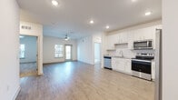 This well-appointed single-floor unit offers a clean, modern aesthetic throughout, defined by light wood-style flooring, crisp white walls, and recessed lighting. The open-concept layout seamlessly connects the living area and kitchen, creating a bright, airy atmosphere. The living space is equipped with a ceiling fan and benefits from natural light through a sliding glass door that leads to an outdoor balcony or patio area.

The kitchen is thoughtfully designed with white shaker-style cabinetry, granite-look countertops, a subway tile backsplash, and a full suite of stainless steel appliances, including a side-by-side refrigerator with ice and water dispenser, electric range, over-the-range microwave, and dishwasher.

The primary bathroom features a dual-sink vanity with granite countertops, a glass-enclosed walk-in shower with tile surround, and wood-style flooring. A secondary bathroom offers a single vanity with matching finishes. Bedrooms are carpeted, with ceiling fans and windows that allow natural light. A dedicated laundry room houses a full-size Whirlpool washer and dryer with overhead wire shelving. Additional storage is provided through a walk-in closet with wire shelving, also carpeted for comfort.