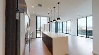 Located in the heart of downtown Tucson at 1 S Church Ave, this contemporary single-floor residence showcases a refined modern design throughout. The open-concept living and kitchen area is anchored by a large central island topped with a crisp white countertop, complemented by dark-toned cabinetry and stainless steel appliances. A cluster of sleek pendant lights hangs overhead, adding an architectural focal point. Light wood-style flooring runs throughout, enhancing the sense of openness and warmth.

Floor-to-ceiling windows and glass sliding doors flood the living area with natural light while framing panoramic views of the Tucson skyline and surrounding mountains. The doors open directly onto a private balcony, extending the living space outdoors.

The primary bathroom features a glass-enclosed walk-in shower, dual undermount sinks set in a long white countertop atop dark floating cabinetry, slate-toned tile flooring, and a large mirror illuminated by pendant lighting. A second bathroom offers wood-look tile flooring, a soaking tub, and a floating vanity with matching dark cabinetry. Together, these spaces reflect a cohesive, contemporary aesthetic suited for urban living in Tucson's vibrant downtown core.