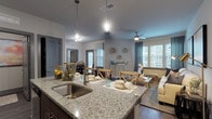 This single-floor residence offers a thoughtfully designed open-concept layout that seamlessly connects the kitchen, dining, and living areas. The kitchen is equipped with stainless steel appliances — including a refrigerator, electric range, and microwave — complemented by rich dark wood cabinetry and granite countertops. A kitchen island with an undermount sink and pendant lighting serves as both a functional workspace and a casual gathering spot. The dining area accommodates a round table and chairs, set atop hardwood-style flooring, with natural light filtering through blinds on a nearby window. The living room features a ceiling fan, large windows with drapery, and ample space for comfortable seating. Two bedrooms are carpeted and well-lit, each offering closet space and windows. The full bathroom includes a granite-topped vanity with dark wood cabinetry, a tiled tub-shower combination, and hardwood-style flooring. A dedicated in-unit laundry room houses a full-sized washer and dryer with overhead shelving. Neutral gray tones and consistent finishes throughout the space create a cohesive, modern aesthetic well-suited for everyday living.