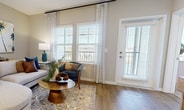 This contemporary apartment in Winter Garden, FL, showcases a thoughtful layout within its 1,110 square feet. The space boasts three bedrooms, including a primary bedroom of 200 square feet, and three full bathrooms. The open-concept living area is a highlight, featuring a stylish living room with large windows that flood the space with natural light. Sheer curtains and plantation shutters offer light control and privacy.

The kitchen is a chef's dream with its sleek white cabinetry, stainless steel appliances, and a generous island with seating for casual dining. Pendant lighting adds a touch of modern elegance. Throughout the apartment, warm wood-toned flooring creates a cohesive look, contrasting beautifully with the light walls and furnishings.

The bedrooms are well-appointed, with the primary bedroom featuring a plush upholstered headboard and ample closet space. Bathrooms are designed with clean lines, featuring modern fixtures and a glass-enclosed shower. An additional office space provides flexibility for work or study.

Attention to detail is evident in the decor, with coastal-inspired artwork, pops of teal and orange, and carefully curated accessories that create a welcoming atmosphere. The apartment's layout efficiently utilizes space, offering both functionality and style in a compact yet comfortable environment.