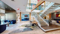 Located at 3044 Hidden Forest Court in Marietta, GA, this thoughtfully designed community space spans a generous footprint across a single floor, offering a dynamic blend of social, collaborative, and functional areas. The entrance opens into a spacious, light-filled lobby anchored by a striking open-tread staircase with glass panel railings and warm wood accents, creating an immediate architectural focal point. Recessed lighting and soaring ceiling heights contribute to an airy, welcoming atmosphere throughout.

The main lounge area is furnished with a contemporary sectional sofa, leather armchairs, a navy ottoman, and a bold black-and-white geometric area rug, bringing together a modern yet inviting aesthetic. Warm wood columns contrast beautifully with crisp white walls and light hardwood-style flooring. Curated artwork and sculptural décor add personality to the space.

A dedicated meeting and workspace room features vibrant blue carpet, workstations with wall-mounted displays, and an abundance of natural light. An adjacent conference area is enclosed by expansive floor-to-ceiling windows offering serene views of an outdoor pool and lush wooded surroundings, making it ideal for focused work or small group meetings. Together, these areas create a versatile and visually cohesive environment suited for both community gatherings and productivity.