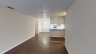 This single-floor residential unit offers a functional and straightforward layout designed for comfortable everyday living. The open-concept living and dining area is finished with rich, dark hardwood-style flooring that extends throughout the main living spaces, complemented by neutral-toned walls and a textured ceiling. A large sliding glass door with vertical blinds fills the living area with natural light and provides access to an outdoor space.

The kitchen is positioned adjacent to the living area, separated by a peninsula counter topped with dark granite-style countertops. White cabinetry lines the walls, accompanied by white appliances including a refrigerator and electric range. A dedicated laundry area is accessible directly from the kitchen, adding notable convenience. A pendant light fixture overhead provides focused task lighting.

The unit includes two bedrooms, both carpeted for comfort and featuring neutral walls and textured ceilings. Each bedroom benefits from natural light via windows fitted with vertical blinds. One bedroom includes a built-in closet with bifold doors, while the other offers direct access to an adjoining room. The bathrooms are fitted with hardwood-style flooring, full tub-shower combos with tiled surrounds, and clean white fixtures throughout, providing a practical and well-maintained finish.