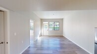 Located at 12730 Monte Vista in Poway, Unit #217 is a thoughtfully designed single-floor residence that blends clean, contemporary finishes with an open, airy feel. Throughout the main living areas, light-toned hardwood-style flooring creates a seamless, cohesive aesthetic that reflects the abundant natural light streaming in through large black-framed windows. The spacious living area features vaulted ceilings that amplify the sense of openness, with direct access to an exterior door framed by a transom window, providing pleasant views of surrounding greenery and landscaping. The bedrooms are well-proportioned and sun-filled, each offering large windows that frame picturesque views of the surrounding hillside and lush foliage — an inviting natural backdrop that enhances the peaceful ambiance. The kitchen is outfitted with rich dark-stained cabinetry, light countertops, stainless steel appliances including a refrigerator and microwave, and a functional sink — offering both style and practicality. The bathroom is generously sized and accessibility-friendly, featuring large-format tile flooring, an open vanity with a wide mirror, and a roll-in shower with grab bars and decorative tile accents. The overall design of the unit emphasizes clean lines, neutral tones, and practical functionality throughout.
