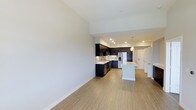 This single-floor residence at Carmel Creek in San Diego offers a thoughtfully designed open-concept layout that seamlessly connects the living area and kitchen. The space is characterized by clean lines and a bright, neutral palette, with light-toned wood-style flooring running throughout that adds warmth while maintaining a contemporary aesthetic.

The kitchen is a standout feature, showcasing dark espresso cabinetry that creates a bold contrast against the light countertops and neutral walls. A mosaic tile backsplash adds a layer of texture and visual interest, while stainless steel appliances lend a polished, modern touch. A central kitchen island with pendant lighting above serves as both a functional workspace and a natural gathering point. Recessed lighting throughout the kitchen ensures the area is well-lit and practical.

The open living area is generously proportioned, offering flexibility for various furniture arrangements. The smooth, light-colored walls and high ceilings contribute to an airy, spacious feel. A hallway visible in the background leads to additional areas of the unit, maintaining a logical and efficient flow. Overall, the space presents a clean, move-in ready environment with modern finishes suited to contemporary living.