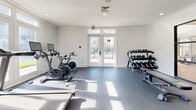 Located at 8340 N Tryon St in Charlotte, North Carolina, this fitness center offers a well-appointed, single-room workout facility designed to support a comprehensive exercise routine. The space features durable rubber-tile flooring throughout, providing a safe and functional surface for a wide range of activities. Recessed lighting and crown molding along the ceiling lend a clean, polished aesthetic to the room.

Natural light floods the interior through large, multi-pane windows and glass-paneled double doors, which open to an outdoor view and lend an open, airy feel to the space. The cardio zone is equipped with multiple treadmills and stationary cycling bikes, each featuring individual console screens for an enhanced workout experience. A dedicated free weights area includes a multi-tiered dumbbell rack stocked with a full range of weights, accompanied by an adjustable workout bench.

A functional training station rounds out the equipment offerings, featuring a wall-mounted rack loaded with medicine balls, kettlebells, resistance bands, TRX suspension trainers, and a stability ball, catering to strength, balance, and flexibility training. The overall ambiance is bright, clean, and modern, creating an inviting environment well-suited for residents seeking convenient, on-site fitness amenities.