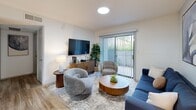 Located at 9024 Northgate Blvd in Austin, TX, this single-story, one-bedroom, one-bathroom unit offers a well-organized layout that maximizes every square foot. The combined living, dining, and kitchen area forms the heart of the home, where wood-style flooring runs throughout and neutral walls create a bright, cohesive atmosphere. The living room features a sliding glass door with vertical blinds, allowing natural light to filter in while providing direct access to an outdoor area. The dining nook is defined by a large wall mirror that visually expands the space and reflects additional light from the adjacent living room. The galley-style kitchen is equipped with white cabinetry, light quartz countertops, a stainless steel sink, and black appliances including an electric range and refrigerator. A hallway connects the main living area to the private bedroom, which is comfortably sized and includes a ceiling fan, a window dressed with sheer curtains and blinds, and a dedicated closet. The bathroom presents a clean, white aesthetic with a single-vanity, white cabinetry, a large mirror with overhead lighting, and a full tub-shower combination with wood-style flooring completing the space. The unit also includes a hallway for added storage transition between rooms.