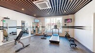 Located at 821 East Main Street in Stamford, Connecticut, Lafayette Fitness Club is a thoughtfully designed exercise room that maximizes its single-floor footprint to deliver a complete fitness experience. The space is defined by its striking architectural ceiling, featuring dark slatted wood panels that lend a modern, sophisticated aesthetic throughout. Bold horizontal stripe accents along the white walls add a dynamic visual rhythm, reinforcing the energetic atmosphere of the club.

The fitness floor is finished with durable, textured rubber-style flooring suited for high-activity use. Equipment includes a treadmill, stationary bike, rowing machines, and a weight bench, alongside a well-stocked dumbbell rack and medicine balls, providing a well-rounded mix of cardio and strength training options. Wall-mounted flat-screen televisions offer entertainment and connectivity during workouts.

A bank of full-length mirrors along one wall expands the sense of space and allows users to monitor their form. A large street-facing window floods the room with natural light and offers views of the vibrant East Main Street corridor below. Efficient ceiling-mounted climate control ensures comfort year-round. The Lafayette Fitness Club branding is prominently displayed in a bold neon-style logo, completing the polished, purposeful character of this urban fitness facility.