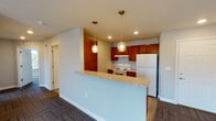 Located in Kokomo, Indiana, this single-floor unit offers a practical and well-appointed layout designed for comfortable everyday living. The open-concept kitchen is a central highlight, featuring warm-toned wood cabinetry, a white electric range, a full-size refrigerator, a stainless sink, and light stone-look countertops. A peninsula breakfast bar with pendant lighting above creates a natural transition into the living area, making the space feel connected and functional. The kitchen is finished with wood-look plank flooring, adding warmth and easy maintenance underfoot. The living and bedroom areas are carpeted with a patterned tile-style carpet that adds texture and visual interest throughout. Bedroom spaces are well-sized, with at least one room featuring a ceiling fan with lighting and a window that brings in natural light. Recessed lighting is present in multiple rooms, providing consistent illumination. The bathroom is thoughtfully updated with a dark espresso vanity, a white countertop, a framed mirror, modern light fixtures, and wood-look flooring. Clean neutral gray walls are consistent throughout the unit, creating a cohesive and move-in ready aesthetic. A private entry door provides direct access to the unit.