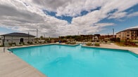 Located at 780 Doss Dr in Marysville, Ohio, this two-floor residential community is designed to offer a modern lifestyle with a strong emphasis on outdoor amenity spaces. The centerpiece of the property is a generously sized resort-style swimming pool with crystal-clear turquoise water, surrounded by a spacious concrete deck lined with green lounge chairs and sun loungers. Adjacent to the main pool is a shallow wading pool featuring in-water chaise lounges, perfect for relaxing in a more leisurely setting.

The outdoor area is thoughtfully landscaped with ornamental grasses, colorful seasonal plantings, and decorative rock beds that add texture and visual interest throughout. A rustic wooden pergola provides a shaded gathering space with seating, creating an inviting retreat within the open-air environment. The clubhouse structure, finished in light stone and board-and-batten siding, anchors one end of the pool deck with large glass doors that connect the interior to the outdoor amenity space.

Black iron fencing encloses the pool area while maintaining open sightlines to the surrounding Ohio landscape and the multi-story residential buildings beyond. The overall ambiance is clean, contemporary, and community-focused, offering residents a well-appointed outdoor retreat suited for both relaxation and social gatherings.
