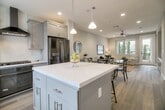 Located at 290 S Main St in Milpitas, California, this three-story model home showcases thoughtful design and high-quality finishes throughout each level. The entry staircase features elegant wrought iron balusters with ornamental detailing and warm wood-toned flooring, setting the tone for the home's refined aesthetic.

The main living area is bright and open, with light hardwood floors, neutral gray walls, and multiple windows that invite natural light from multiple directions. A ceiling fan anchors the central gathering space, which flows seamlessly into a well-appointed dining area with views of the surrounding neighborhood.

The kitchen is a standout feature, boasting an expansive quartz waterfall island with seating, white shaker cabinetry, a geometric tile backsplash, a professional-grade range hood, and pendant lighting overhead. A full suite of black stainless appliances completes the space.

Bedrooms are generously sized with large windows offering ample natural light. The primary bathroom impresses with marble-look tile flooring, a dual-sink vanity with brushed gold fixtures, and a glass-enclosed walk-in shower. Additional cabinetry areas provide abundant built-in storage with clean white shaker-style cabinets and quartz countertops. This model home exemplifies contemporary living in the heart of Milpitas.