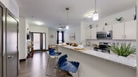 This thoughtfully designed one-bedroom, one-bathroom apartment on the third floor at 640 E Michigan Street offers a functional and modern living experience. The open-concept kitchen and living area forms the heart of the unit, where the kitchen stands out with white cabinetry, a white subway tile backsplash, stainless steel appliances including a refrigerator, electric range, and microwave, and a generous granite-topped island with bar seating illuminated by pendant lighting. The kitchen flows seamlessly into the living room, which features wood-style flooring, a ceiling fan, and access to a glazed exterior door that brings in natural light. Multiple windows dressed with blinds and curtains allow daylight to filter throughout the space. The bedroom is carpeted for comfort and includes a ceiling fan, windows providing natural light, and ample room for a full furniture arrangement. The bathroom is clean and straightforward, featuring a shower-tub combination with a curtain, wood-style flooring, and crisp white walls. A dedicated in-unit laundry area houses a full-size top-load washer and dryer with shelving above, adding notable convenience to everyday living.
