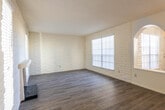 This two-story space is defined by a distinctive architectural character, most notably its painted white brick walls that appear consistently throughout both levels, lending a cohesive and textural quality to the interior. The main living area on the ground floor is generously sized, featuring wood-look plank flooring, multiple windows with horizontal blinds that allow ample natural light, and a wood-burning fireplace serving as a focal point. A textured ceiling adds depth overhead.

The entry level also includes a functional kitchen equipped with gray cabinetry, a dishwasher, refrigerator, and a window above the sink that brings in natural light. The kitchen connects seamlessly to the main living and dining areas via wood-look flooring that flows throughout the lower level.

A white-railed staircase with elegant arched doorway details leads to the upper floor, where the bedrooms are located. Each bedroom features plush carpeting, ceiling fans, painted brick accent walls, and windows with blinds. Closet access is available in the bedrooms, providing practical storage. The bathroom includes a full tub-shower combination with tiled surround and a window for ventilation and natural light. Overall, the space presents a warm, character-rich environment with consistent finishes across both floors.