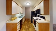 Located at 15300 37th Ave N in Plymouth, Minnesota, this single-floor residence offers a functional and comfortable layout throughout. The galley-style kitchen is well-equipped with white cabinetry featuring wood-tone accents, generous upper and lower storage, wood-look flooring, a double-basin sink, and black appliances including a refrigerator, electric range, and microwave. The living area is a standout feature of the home, showcasing soaring vaulted ceilings, a ceiling fan, a raised-hearth fireplace with glass surround, and large vertical-blind-covered windows that bring in natural light. Soft carpeting flows through the living space and into the bedrooms, each of which features windows with outdoor views, baseboard heating, and ample closet access via warm wood-toned doors. A hallway connects the bedroom areas to the full bathroom, which includes a tiled tub and shower combination, a vanity with storage, tiled flooring, and a towel bar. Textured ceilings are consistent throughout the home, adding a classic residential feel. The overall layout is efficient and well-organized, providing comfortable living within a quiet Plymouth neighborhood setting.