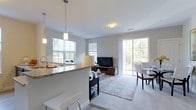This well-appointed 2-bedroom, 2-bathroom residence is designed with modern living in mind, offering an open-concept floor plan that seamlessly connects the kitchen, living, and dining areas. The kitchen features a granite-topped breakfast bar with pendant lighting overhead, providing both a functional workspace and a casual dining spot. Soft neutral tones on the walls and plush carpeting throughout the living area create a warm and inviting atmosphere. Large windows and a sliding glass door flood the space with abundant natural light while offering views of the greenery outside, enhancing the sense of openness. The living area comfortably accommodates a sitting arrangement centered around a media console, while the adjacent dining space offers room for a full dining set. The layout flows intuitively across the single floor, making everyday living both convenient and comfortable. Clean architectural lines, recessed and flush-mount lighting, and cohesive finishes contribute to the overall polished aesthetic. This thoughtfully designed residence balances style and practicality, making it an ideal home for those seeking a bright, contemporary living environment.