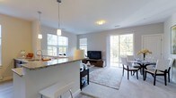 This well-appointed 2-bedroom, 2-bathroom residence is designed with modern living in mind, offering an open-concept floor plan that seamlessly connects the kitchen, living, and dining areas. The kitchen features a granite-topped breakfast bar with pendant lighting overhead, providing both a functional workspace and a casual dining spot. Soft neutral tones on the walls and plush carpeting throughout the living area create a warm and inviting atmosphere. Large windows and a sliding glass door flood the space with abundant natural light while offering views of the greenery outside, enhancing the sense of openness. The living area comfortably accommodates a sitting arrangement centered around a media console, while the adjacent dining space offers room for a full dining set. The layout flows intuitively across the single floor, making everyday living both convenient and comfortable. Clean architectural lines, recessed and flush-mount lighting, and cohesive finishes contribute to the overall polished aesthetic. This thoughtfully designed residence balances style and practicality, making it an ideal home for those seeking a bright, contemporary living environment.