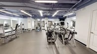 Located at 227 Church St in New Haven, CT, this fitness facility offers a generously sized, single-floor workout space designed to accommodate a wide variety of exercise needs. The gym features an industrial-style aesthetic, with an exposed ceiling showcasing painted ductwork and structural elements overhead, complemented by bright fluorescent strip lighting that ensures the space is well-lit throughout.

The flooring consists of durable rubber matting, providing both safety and comfort during workouts. Large wall-mounted mirrors are strategically positioned throughout the space, enhancing the sense of openness and allowing users to monitor their form during exercise.

The cardio section is well-stocked with multiple treadmills, elliptical machines, a rowing machine, and a stationary bike, catering to a range of cardiovascular training preferences. The strength training area features a multi-station cable machine, a variety of selectorized weight machines targeting different muscle groups, adjustable benches, and a medicine ball rack. A BOSU balance trainer adds a functional fitness dimension to the facility.

Structural columns punctuate the open floor plan, while white-painted walls keep the environment feeling clean and focused. A water cooler station and a wall-mounted television add to the overall convenience of the space, making this gym a comprehensive and practical fitness destination.