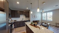 This single-story residence offers a thoughtfully designed open-concept layout that seamlessly connects the kitchen, dining, and living areas. The kitchen serves as a central feature, showcasing dark espresso cabinetry extending to the ceiling, light granite countertops, a large center island with seating, stainless steel appliances, a subway tile backsplash, and pendant lighting overhead. Wood-style flooring flows throughout the main living areas, enhancing the warm, cohesive aesthetic.

The living and dining areas benefit from generous natural light provided by multiple windows with horizontal blinds, complemented by ceiling fans and a decorative globe pendant fixture. A door leads to an outdoor area, further brightening the space.

The bedrooms feature plush carpeting, ceiling fans, and large windows that invite natural light and outdoor views. The primary bedroom is spacious enough to accommodate a substantial headboard and furnishings comfortably.

The bathroom includes a dual-sink vanity with white quartz countertops, brushed nickel fixtures, and a large framed mirror, delivering a clean, modern aesthetic. Overall, the residence combines functional design with contemporary finishes to create a comfortable and inviting living environment.