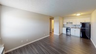 This single-floor unit offers a straightforward and functional layout designed for comfortable everyday living. Dark hardwood-style flooring runs throughout the space, providing a cohesive and modern look that contrasts cleanly with the light gray walls and bright white baseboards.

The living area is open and well-proportioned, with a textured ceiling and a front entry door that includes a sidelight window, allowing natural light to filter in. The space connects seamlessly to the kitchen, which is equipped with white cabinetry, granite-style countertops, a double-basin stainless steel sink, a gas range, and a full-size black refrigerator. A closet adjacent to the kitchen adds convenient storage.

The bedroom is a quiet, private space featuring a ceiling fan with integrated lighting and a window fitted with white blinds that provides natural light and ventilation. The neutral wall tones and consistent flooring keep the room feeling cohesive with the rest of the unit.

The bathroom is efficiently designed, featuring a stand-alone walk-in shower with a chrome showerhead and curtain rod, a toilet, and a granite-style vanity surface. The soft gray walls and clean white fixtures give the bathroom a simple, tidy aesthetic. Overall, the unit presents a clean, move-in-ready environment with updated finishes throughout.