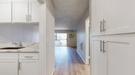 Located at 9901 Lurline Ave in the Chatsworth neighborhood of Los Angeles, this generously sized single-floor residence offers a well-designed layout with an entrance, a large living room, and two full bathrooms. The interior is finished with light wood-style flooring throughout, complemented by neutral gray walls and textured ceilings that add depth to each room. The open-concept living area is bright and expansive, flowing naturally from the entrance toward a pass-through kitchen featuring white cabinetry with modern brushed nickel hardware and a sleek marble-style countertop. A wall-mounted heating and cooling unit provides climate control convenience. The living room is anchored by a sliding glass door that opens onto a private balcony, offering views of the landscaped courtyard below, lined with palm trees and drought-tolerant plantings. Both bathrooms are finished with wood-look flooring and clean white fixtures; one includes a full tub-shower combination with brushed nickel fittings, while another features a wide vanity with a marble-style countertop, a large mirror, and a spacious sliding-door closet. The overall ambiance is clean, modern, and move-in ready, reflecting a thoughtfully updated interior in a well-maintained multi-unit community.