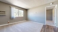 This efficient one-bedroom, one-bathroom unit is thoughtfully arranged across a single floor, making the most of its compact footprint. Neutral gray walls and white trim create a clean, cohesive aesthetic throughout. The living room features a combination of wood-look vinyl flooring and plush carpeting, a window with a window-unit air conditioner, and a baseboard heating system — providing year-round climate comfort. A hallway connects the main living area to the private bedroom and bathroom.

The kitchen is equipped with white shaker-style cabinetry, gray laminate countertops, and a full suite of stainless steel appliances including a range, microwave, and dishwasher. Wood-look vinyl flooring continues here, and a window allows natural light to brighten the space.

The bedroom offers comfortable carpeting, a ceiling fan, a window with views of surrounding greenery, and baseboard heating. A dedicated closet provides practical storage.

The bathroom is finished with wood-look vinyl flooring, a white vanity with ample cabinet storage, and a full tub/shower combo. Textured ceilings are present throughout the unit, adding a classic touch to the overall interior character.