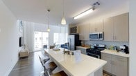 This contemporary two-floor space is designed with a clean, modern aesthetic that emphasizes open living and functional design. The kitchen serves as a central highlight, anchored by a generous white quartz island with bar seating — perfect for casual dining or entertaining. Pendant lighting hangs above the island, adding a refined touch to the space. The kitchen is fully equipped with stainless steel appliances, including a gas range, built-in microwave, and French door refrigerator, complemented by light wood cabinetry, a decorative tile backsplash, and ample storage. A wine rack integrated into the upper cabinetry adds a stylish, practical element. The open layout flows seamlessly into the living area, where large windows and sliding glass doors flood the space with natural light and provide access to an outdoor area, extending the sense of space. Hardwood flooring runs throughout, tying the living and kitchen zones together cohesively. The bright, neutral color palette of whites and light woods creates an airy, welcoming ambiance across both floors, making this a well-appointed space suited for comfortable modern living.