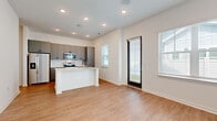 Located at 272 Mazari Ln in Venice, Florida, this well-appointed single-floor home showcases a clean, modern design with consistent light wood-tone flooring and crisp white walls throughout. The open-concept living and kitchen area serves as the heart of the home, featuring a central island with a quartz countertop and undermount sink, sleek gray flat-panel cabinetry, a white subway tile backsplash, and a full suite of stainless steel appliances including a refrigerator, range, and microwave. Recessed lighting and multiple windows allow natural light to flow freely through the space. The bedrooms are generously proportioned with tall ceilings, large windows offering views of the surrounding neighborhood, and ample wall space. The primary bathroom is particularly well-appointed, featuring a long dual-sink vanity with quartz countertops, blue-gray cabinetry, illuminated mirrors, and a glass-enclosed walk-in shower with subway tile surround. A secondary bathroom mirrors the same refined aesthetic. A dedicated laundry closet with a stacked washer and dryer adds everyday convenience. The home's overall ambiance is bright, clean, and contemporary, making it a comfortable and functional residence in the Venice area.