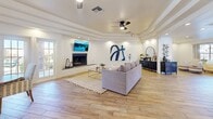 Located at 345 Shadow Mountain Dr in El Paso, TX, this well-appointed single-floor space offers a thoughtfully designed layout encompassing a combined living and dining area along with a dedicated office. Throughout the space, warm wood-look flooring creates a cohesive and inviting aesthetic, complemented by crisp white walls that enhance the bright, airy atmosphere.

The living area is a standout, anchored by a sleek fireplace with a dark surround and a wall-mounted television above it. A tray ceiling with recessed lighting adds architectural depth and a sense of elevated style, while a ceiling fan ensures comfort. Bold abstract wall art adds a modern, curated touch to the lounge setting.

The dining area flows naturally from the living space and is bathed in natural light, thanks to a set of French doors that open to an outdoor area, offering pleasant exterior views. A decorative wooden open shelving unit serves as an elegant room divider, adding warmth and visual interest. Tray ceilings continue here, reinforcing the architectural consistency throughout.

A welcoming reception or lounge area connects the rooms with an open corridor, offering flexible use of the space. The office area is neatly separated, providing a functional and quiet workspace. Together, the rooms create a harmonious, modern environment ideal for gathering, working, and everyday use.