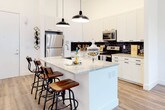 Located at 222 Peters St SW in Atlanta, GA, this single-floor residence offers a thoughtfully designed layout that blends modern aesthetics with functional living. The open-concept kitchen serves as a visual centerpiece, boasting crisp white cabinetry extending to soaring ceiling heights, a striking black subway tile backsplash, stainless steel appliances, and a generous granite-topped island illuminated by pendant lighting — ideal for both cooking and casual dining with bar seating. The living area is warm and inviting, featuring luxury vinyl plank flooring throughout, a curated wall gallery, and a bank of large windows that flood the space with natural light and offer views of the surrounding neighborhood. The bedroom is a serene retreat, comfortably appointed and connected to the rest of the unit with ease. The bathroom continues the home's clean, contemporary aesthetic with granite countertops, white cabinetry with matte black hardware, white subway tile in the tub surround, and a large mirror. Throughout the unit, tall ceilings amplify the sense of openness, and the neutral white walls provide a versatile backdrop. The overall ambiance is polished and modern, reflecting the vibrant character of its Atlanta location.